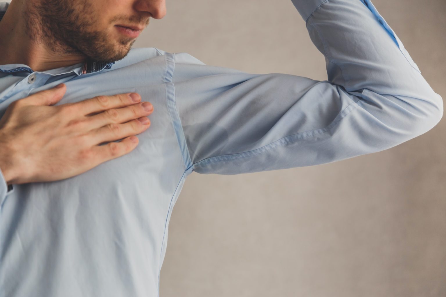 Man with hyperhidrosis sweating very badly under armpit in blue shirt, on grey.