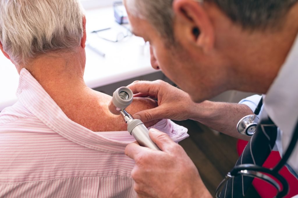 Matured male Caucasian dermatologist examining senior patient through dermatoscopy at clinic